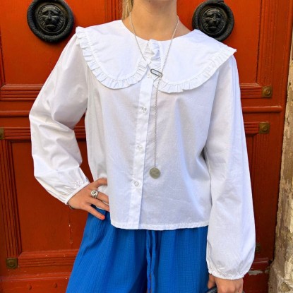 Blouse écolière blanche vue de face et portée par une femme devant une porte rouge