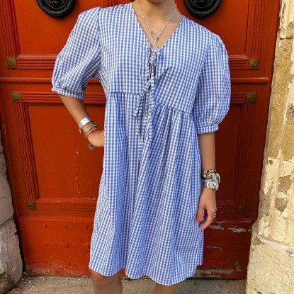 Robe Cassandra à carreaux bleus et blancs vue de face et portée par une femme devant une porte rouge