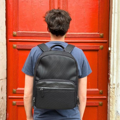 Sac à dos Francinel de couleur noir vue porté sur le dos d'un homme devant une porte rouge