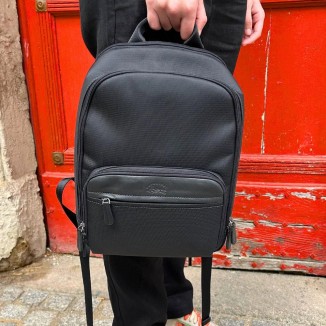 Sac à dos Francinel de couleur noir porté à la main par un homme et vue de face devant une porte rouge